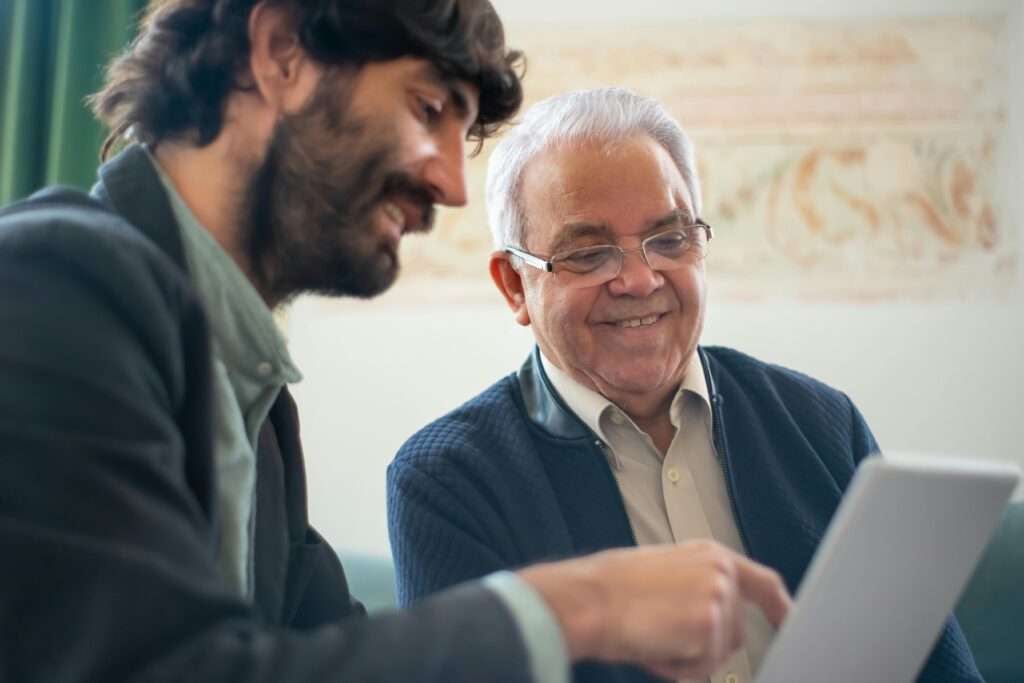 Elderly man discussing business with a younger colleague using a laptop indoors.